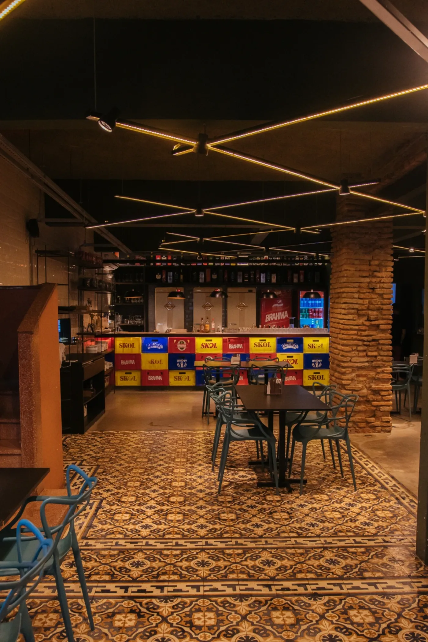Bar com pilar de tijolo aparente, ladrilho hidráulico restaurado e trilhos de luz em zigue-zague