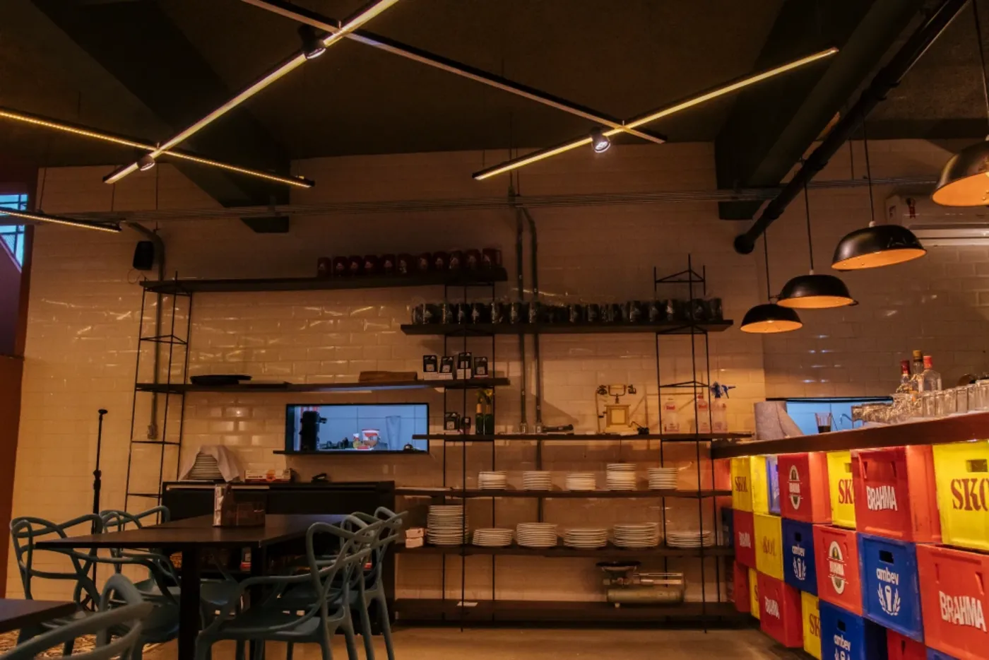 Salão de bar com balcão de engradados, prateleiras metálicas e trilhos de iluminação linear no teto