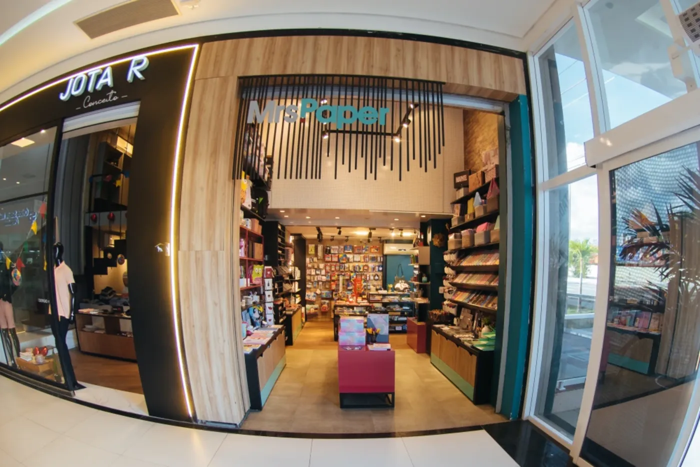 Vitrine de papelaria em shopping, com portal em ripado de madeira, letreiro iluminado e fachada vizinha em preto